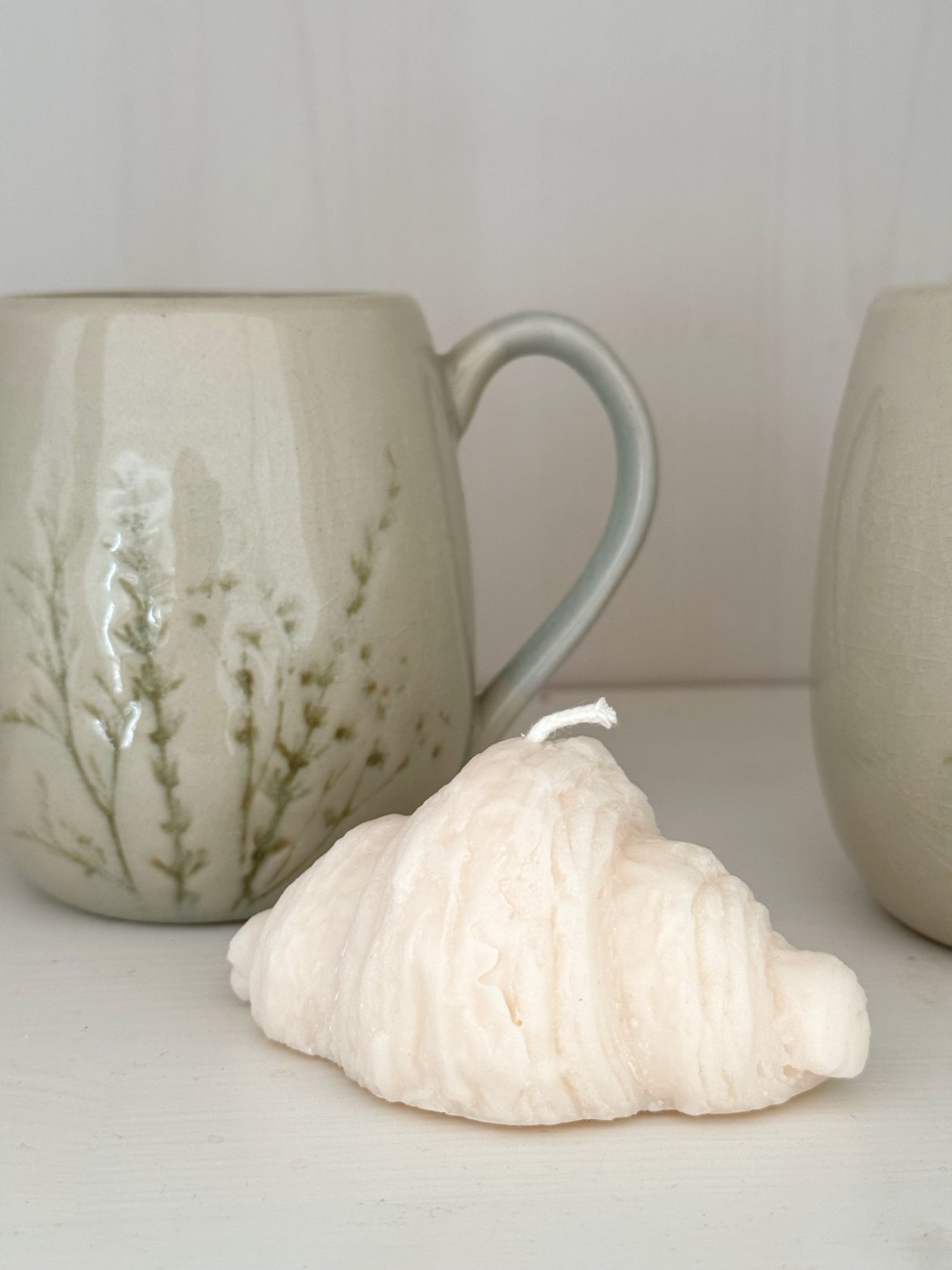 kerze in croissant form vor keramikbecher