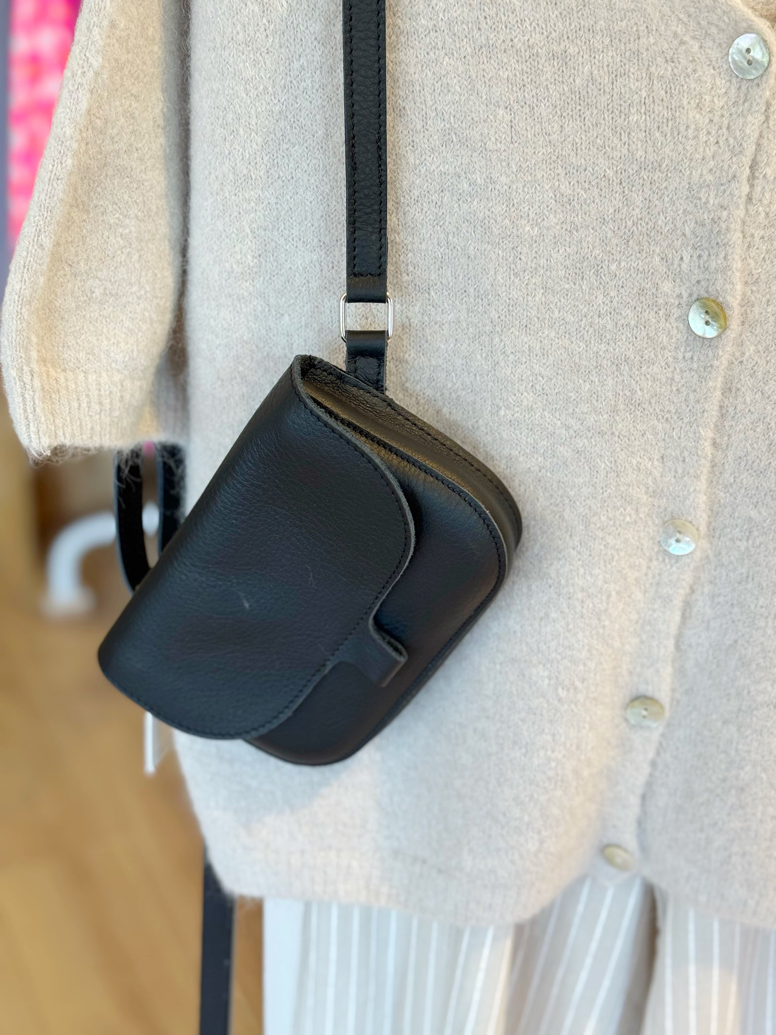 kleine schwarze umhägetasche auf cremefarbenem Oberteil