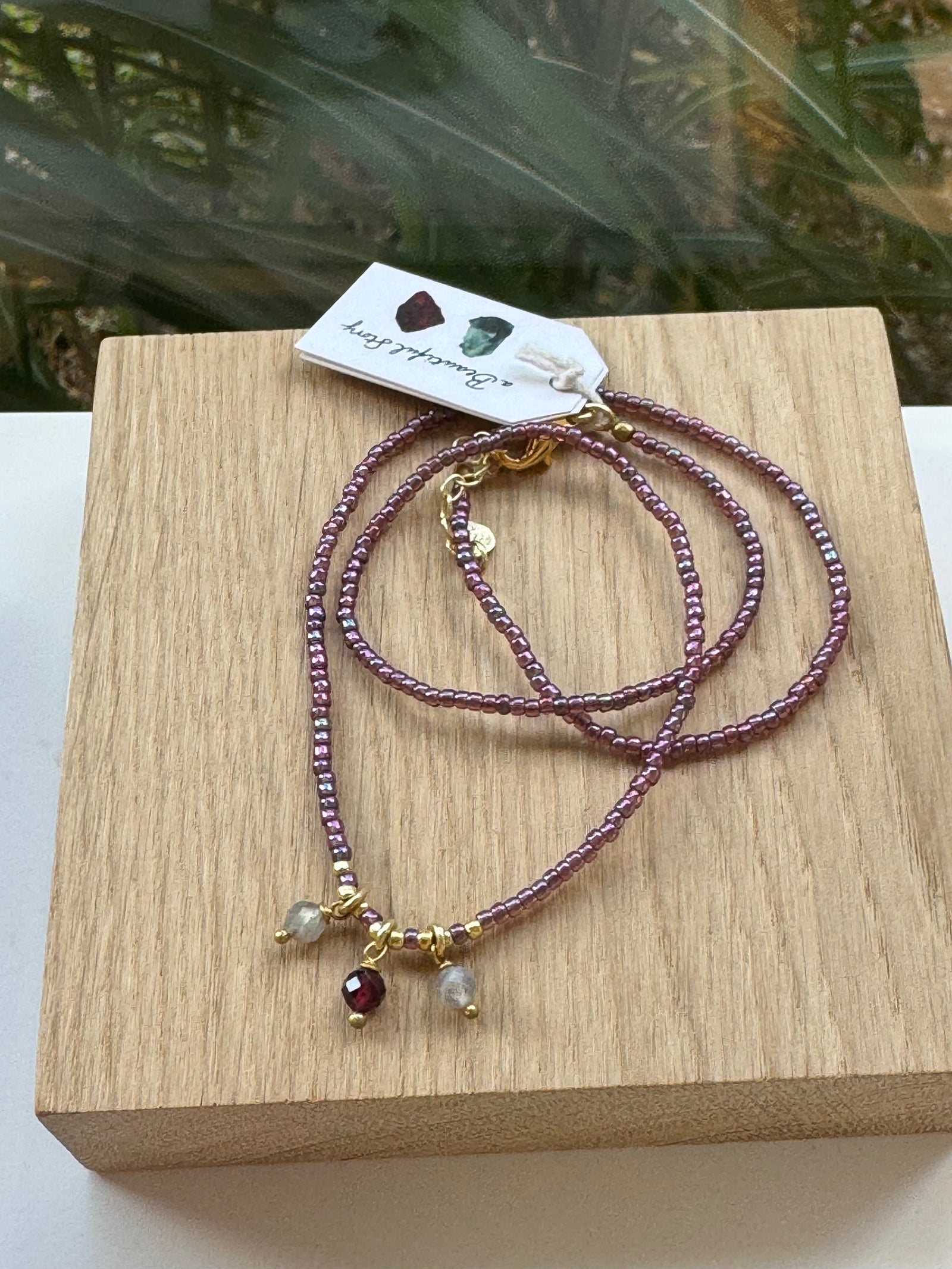 kette mit brombeerfarbenen Glasperlen und Rosenquarz auf Holzplatte