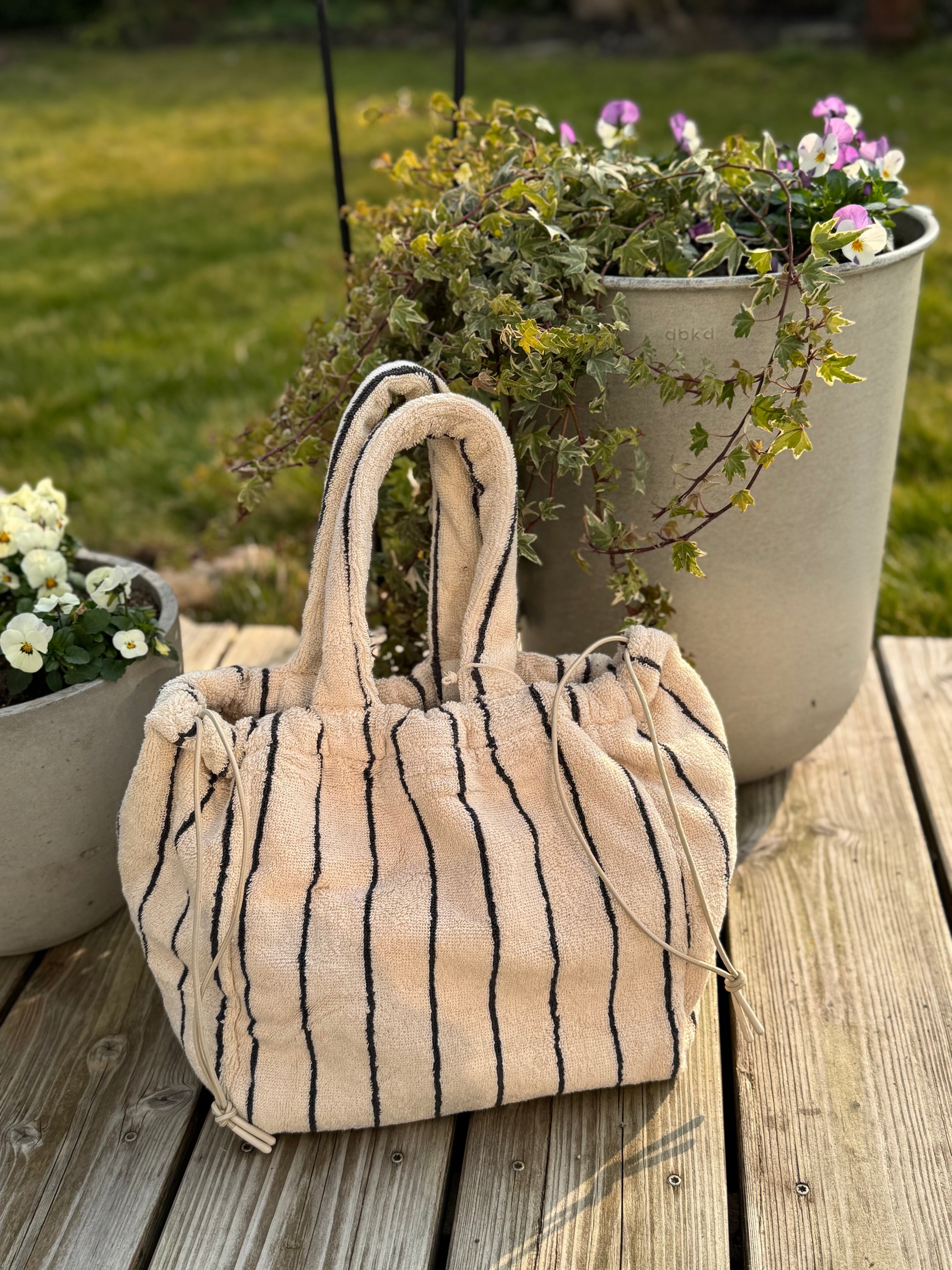 gestreifte Handtasche (creme,schwarz) aus Frottee vor Blumentopf auf Terrasse 
