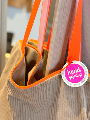 Detailaufnahme eines Shoppers aus sandfarbenen Cord mit orangenem Reisverschluss und Tragegurt