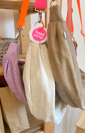 Drei Crossbody Bags aus Cord in den Farben flieder, creme, braun mit Neon Gurten, hängend
