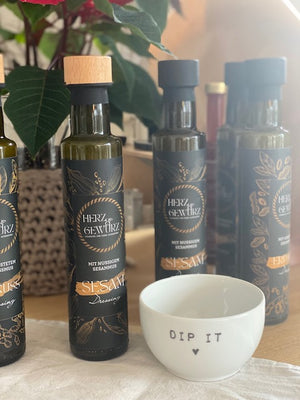 Stimmungsvolles Bild mit mehreren Dressing Flaschen von Herz und Gewürz vor Pflanze. Davor eine weiße, kleine keramikschüssel mit edem Aufdruck "dip". Bei Stadtrandstil Conceptstore