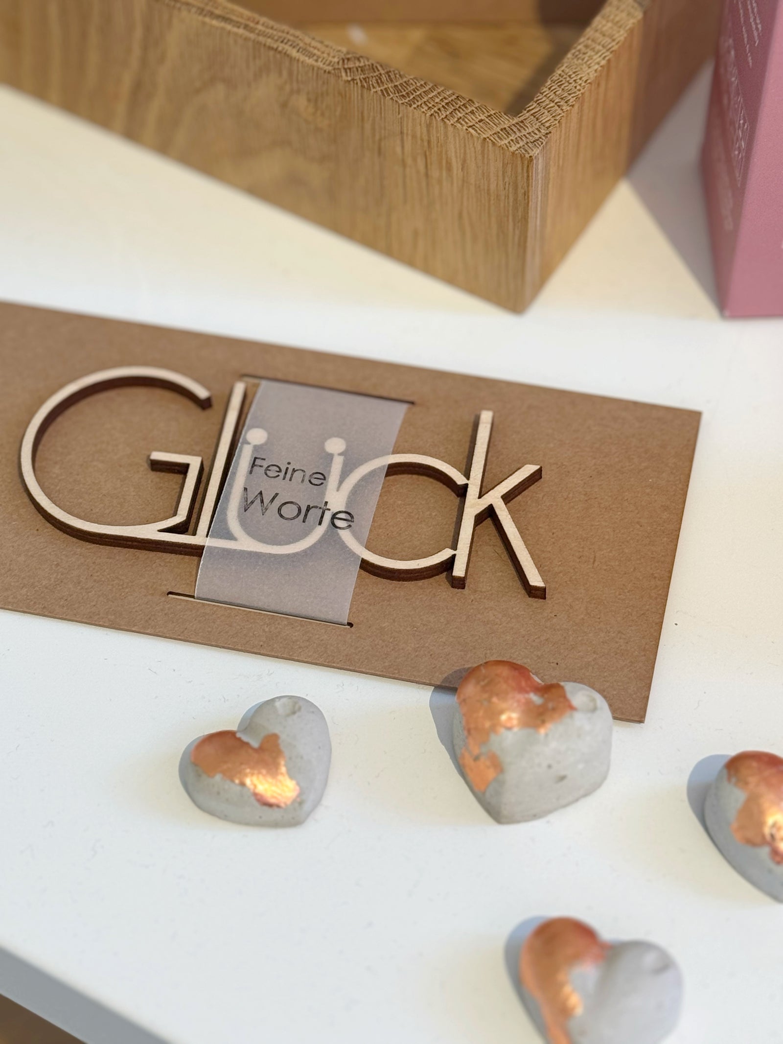 Hübsch dekoriert: ein ovales Beton tablett mt drei Betonherzen mit Blattgold, einem Armband und Schleierkraut. Dhinter steht ein Schriftzug "Liebe" aus Holz, davor ein Schriftzug, liegend "Glück"