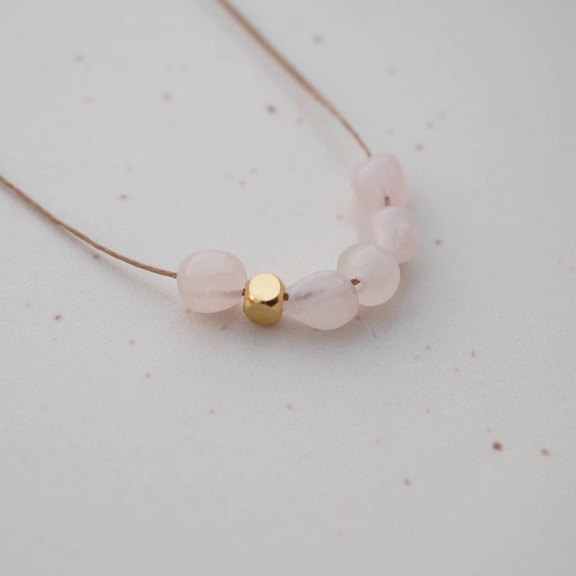 Detailfoto Kette Nala: gewachstes Band mit 5 Rosenquarzperlen und einem goldfarbenem Metallelement
