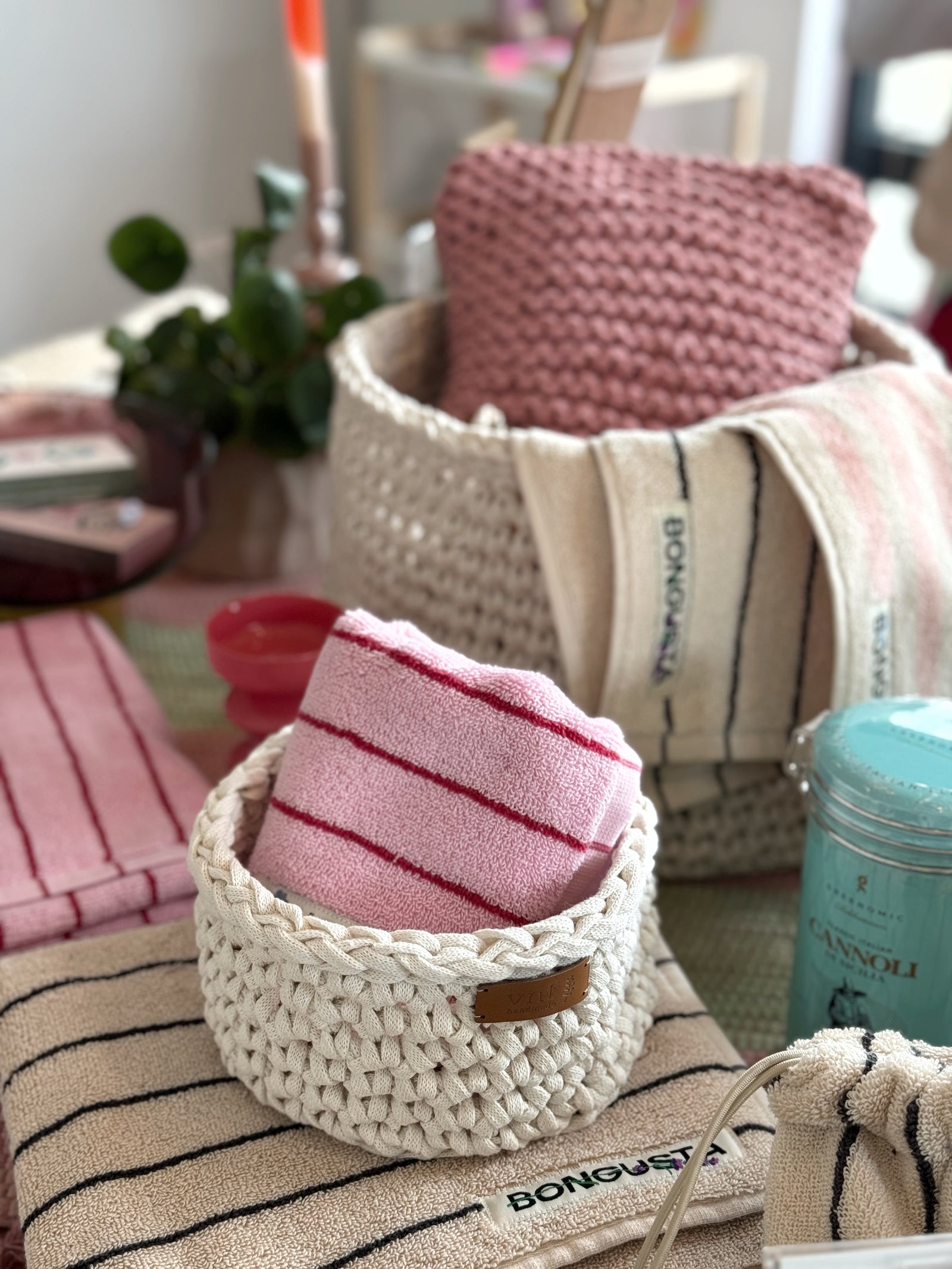 Naturfarbener gehäkelter Korb gefüllt mit einem himbeerfarbenem gestrickten Kissen und einem gestreifte Handuch