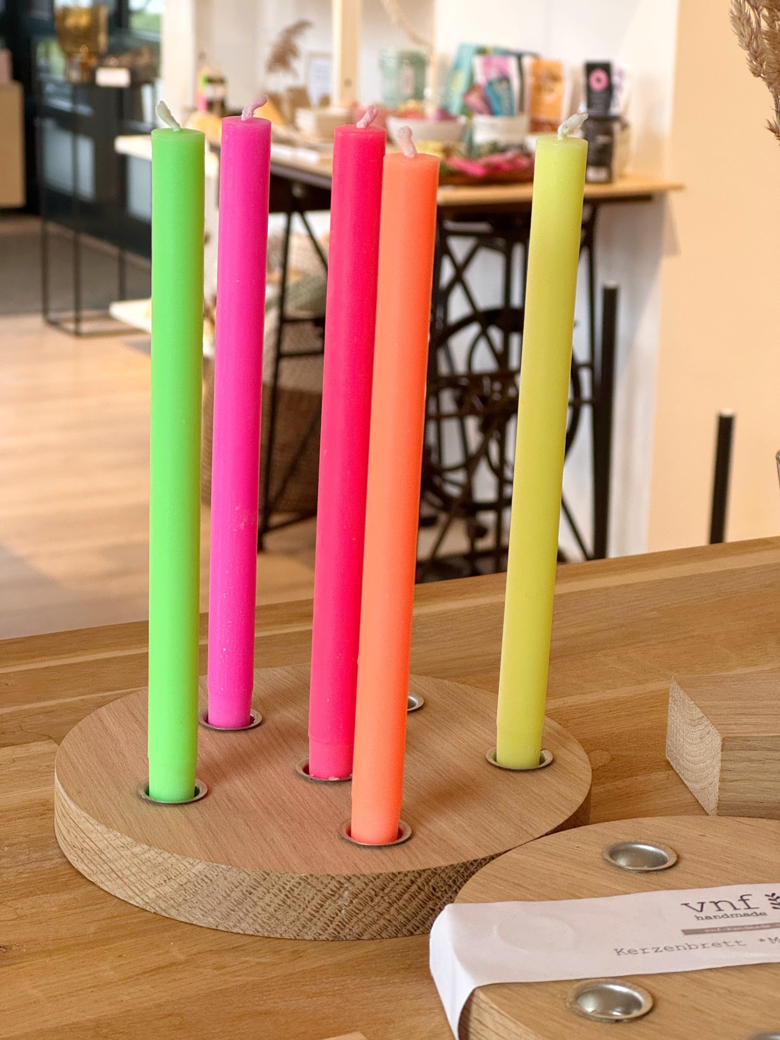 6 neonfarbene Kerzen in einem runden Kerzenteller aus Holz