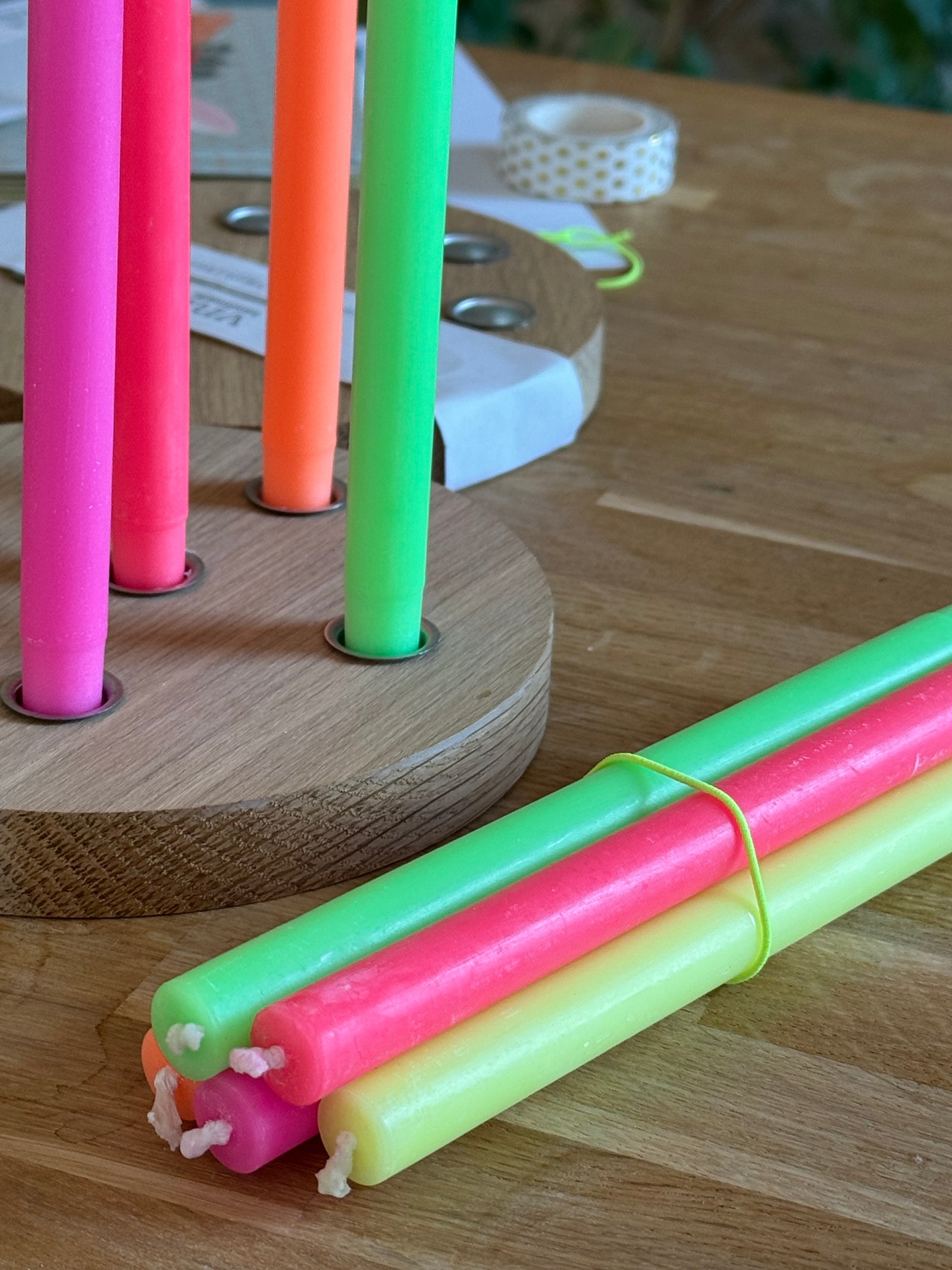 6 neonfarbene Kerzen in einem runden Kerzenteller aus Holz