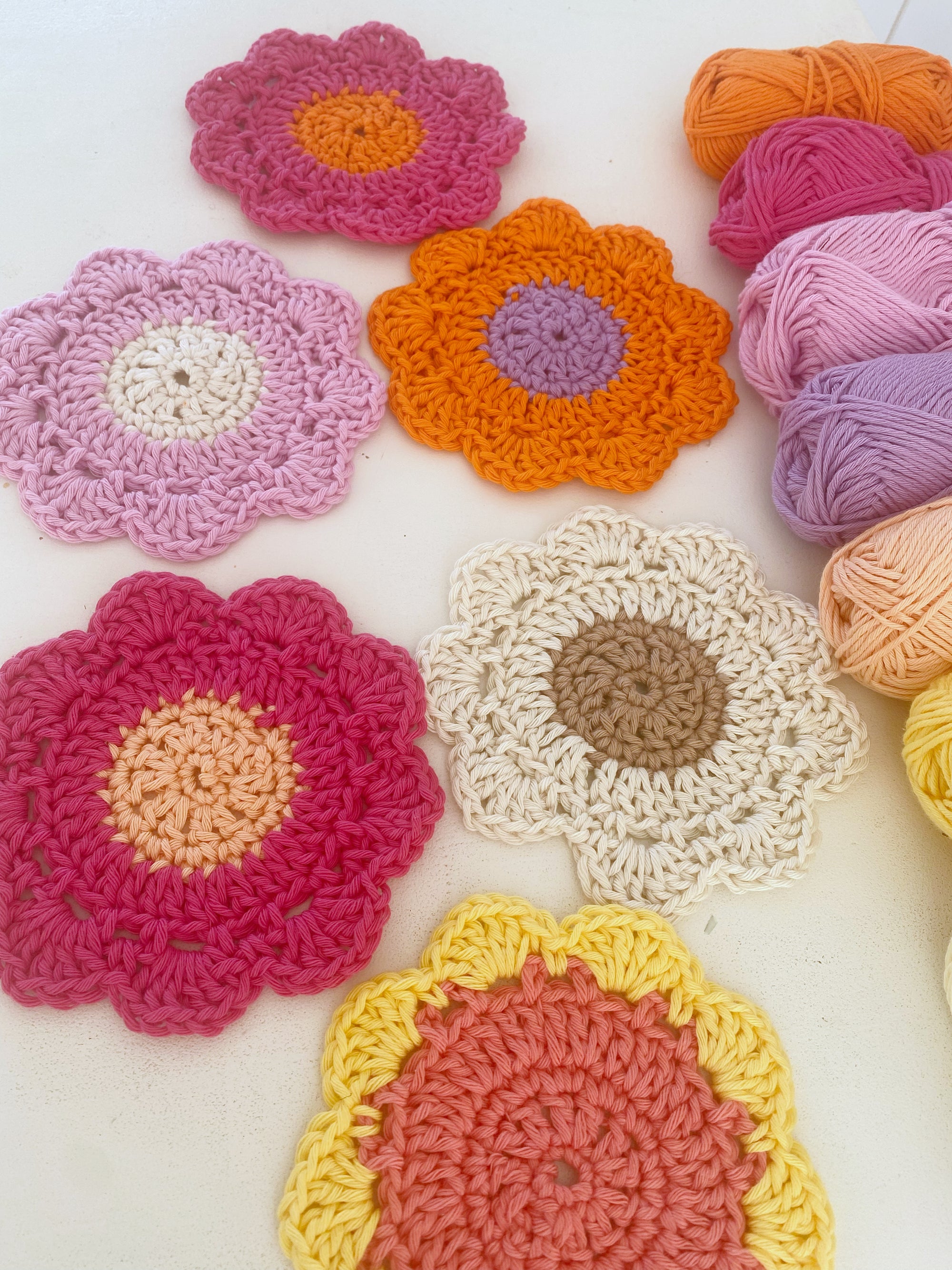 Gartentisch voller bunter Untersetzer in Blumenform, gehäkelt von Stadtrandstil handmade. Auf einem steht eine Tasse mit einem Smiley