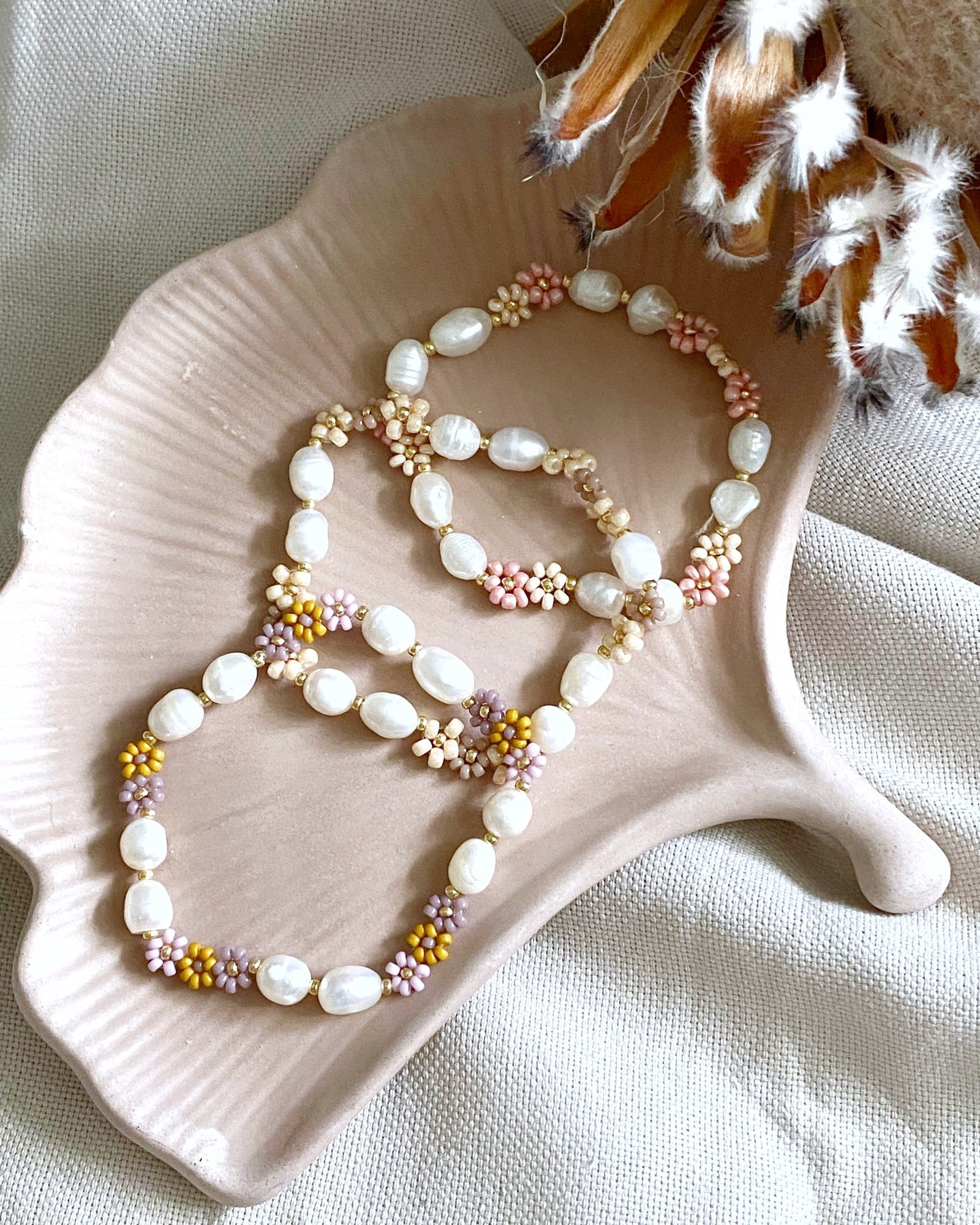 Drei Armbänder mit Süßwasserperlen und blumen auf gingco keramikschale