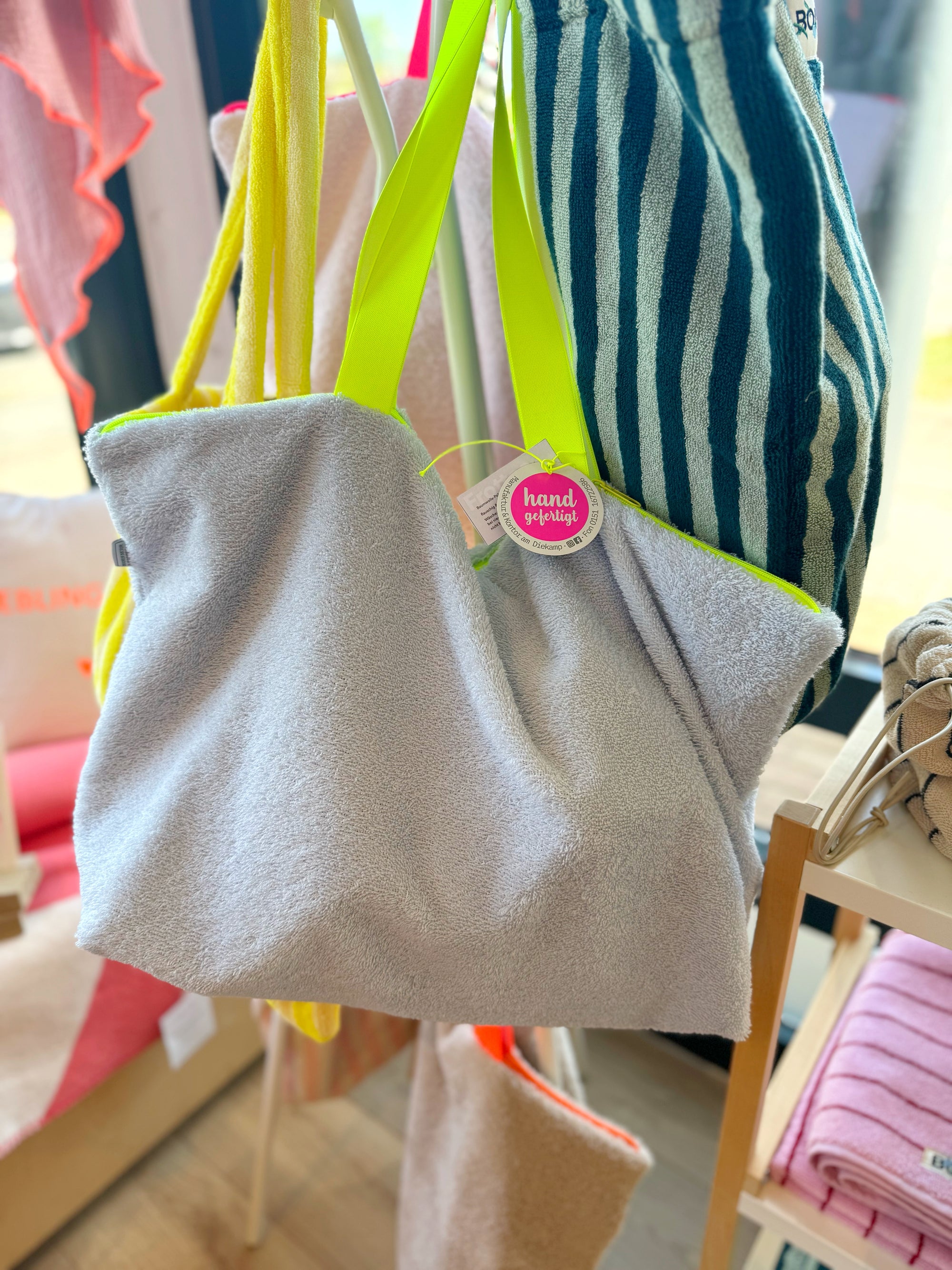 Blassblaue Strandtasche aus Frottee mit neongelbem Gurt auf Taschenständer
