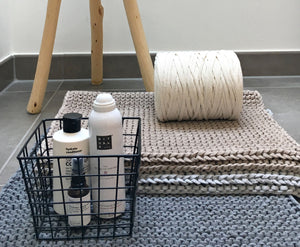 Badezimmer Teppiche in Naturtönen mit einer Rolle des Materials dekoriert und einem Drahtkorb mit Pflegeutensilien. Maerkennt die grobe Struktur des handgearbeitetem Teppichs.