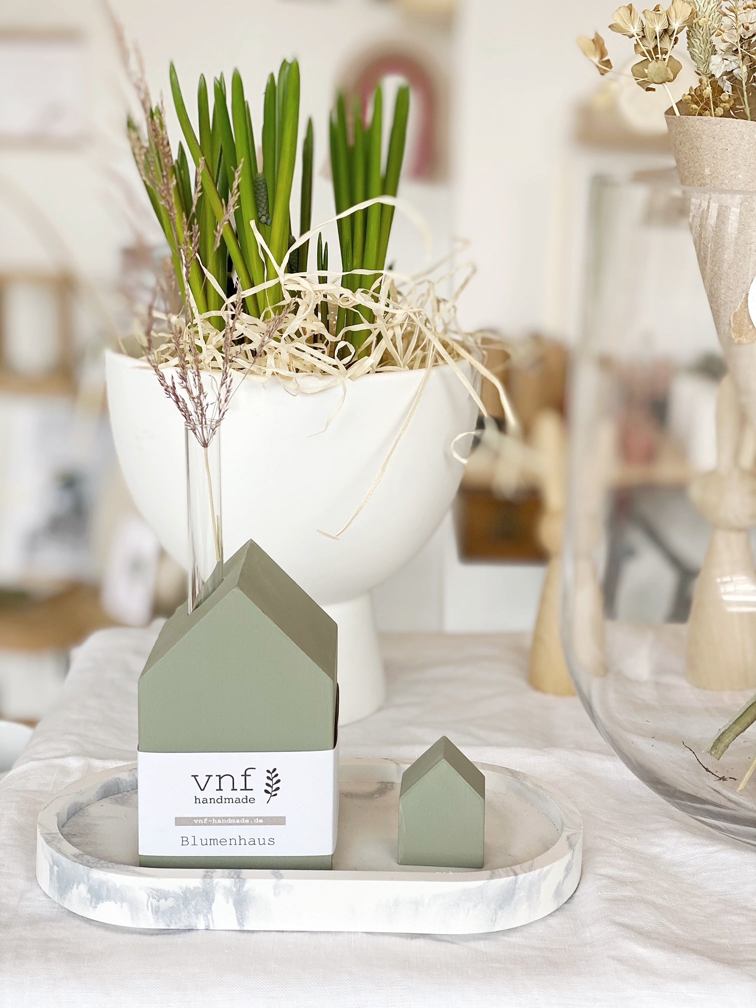 Natürliches Arrangement mit einem handbemaltem Blumenhaus in oliv, einem farblich passendem Minihaus, sowie einer weißen Schale mit Pflanzen, einem marmorierten Tablett und einer Vase