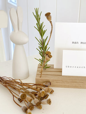 Detailansicht großer Fotohalter aus Eiche von Stadtrandstil mit Bohrungen für Trockenblumen. Dekoriert mit Mohnkapseln und Rosmarinzweig. Daneben ein weißer, stilisierter Holzhase