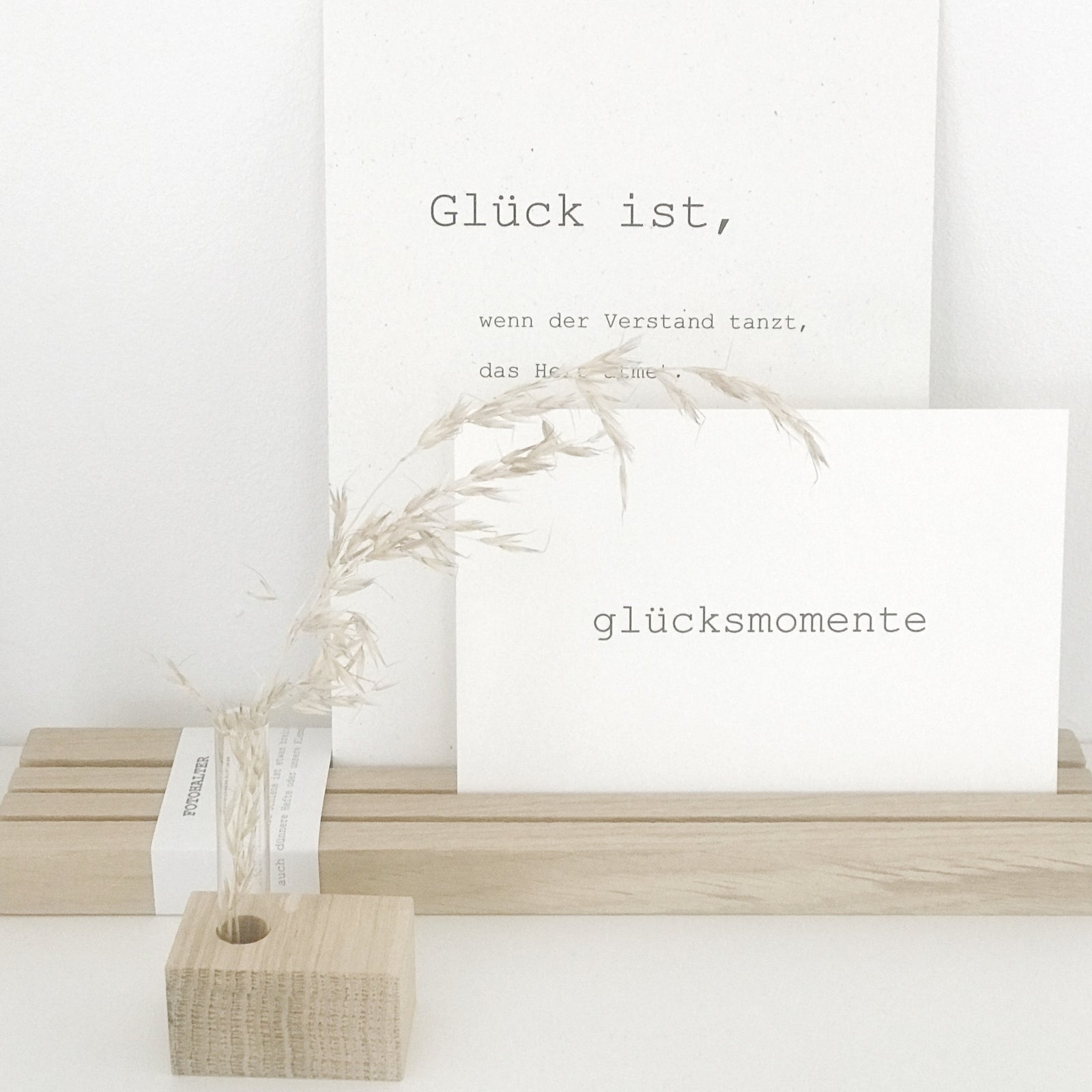 Großer Fotohalter mit drei Rillen von Stadtrandstil. Dekoriert mit einer Postkarte mit dem Aufdruck Glücksmomente und einer A5 Karte mit Text. Davor eine Minivase mit Trockengras.