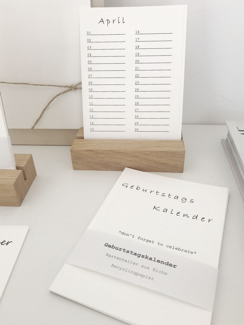 Geburtstagskalender (immerwährend) in minimalistischem Design von Stadtrandstil in Postkartenformat mit einem Halter aus unbehandeltem Eichenholz. Daneben eine Minivase mit getrocknetem Gras.