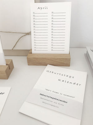 Minimalistischer Geburtstagskalender aus Recyclingpapier mit einem Halter aus Eiche. Davor liegen die Kalenderblätter.
