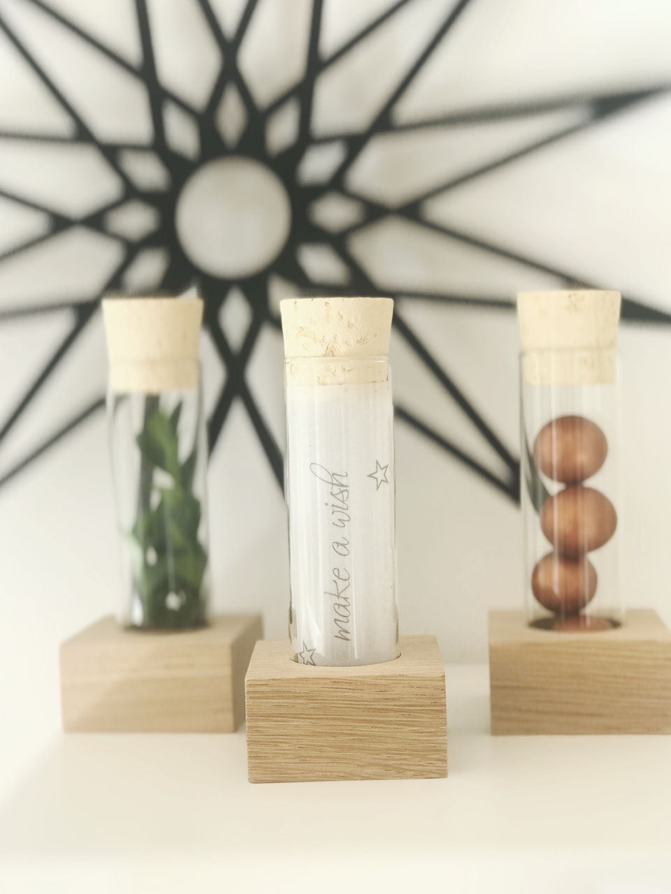 Drei große Reagenzgläser mit Naturkorken in einer Halterung us Eichenholz. Die Gläser sind mit Schokodrops, Trockenblumen und einem Transparentpapier gefüllt. Davor steht ein gelaserter Holz Schriftzug "Danke"