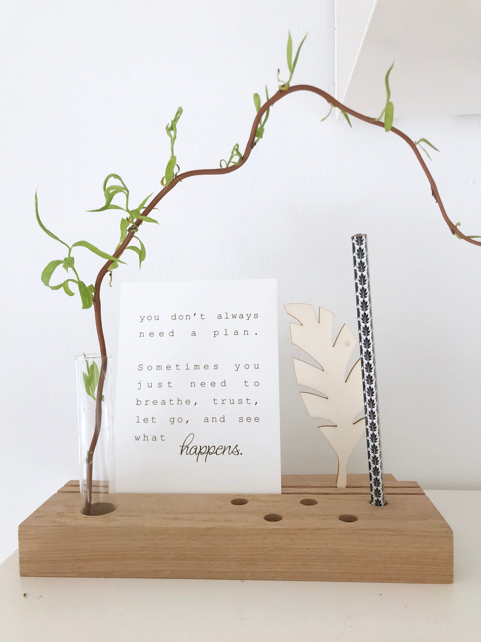 Multifunktionaler Karten-und Stiftehalter mit Platz für ein Reagenzglas, in dem ein Weidenzweig steckt. Dekoriert mit einem Stift, einer Postkarte mit einem Zitat und einer Feder aus Holz