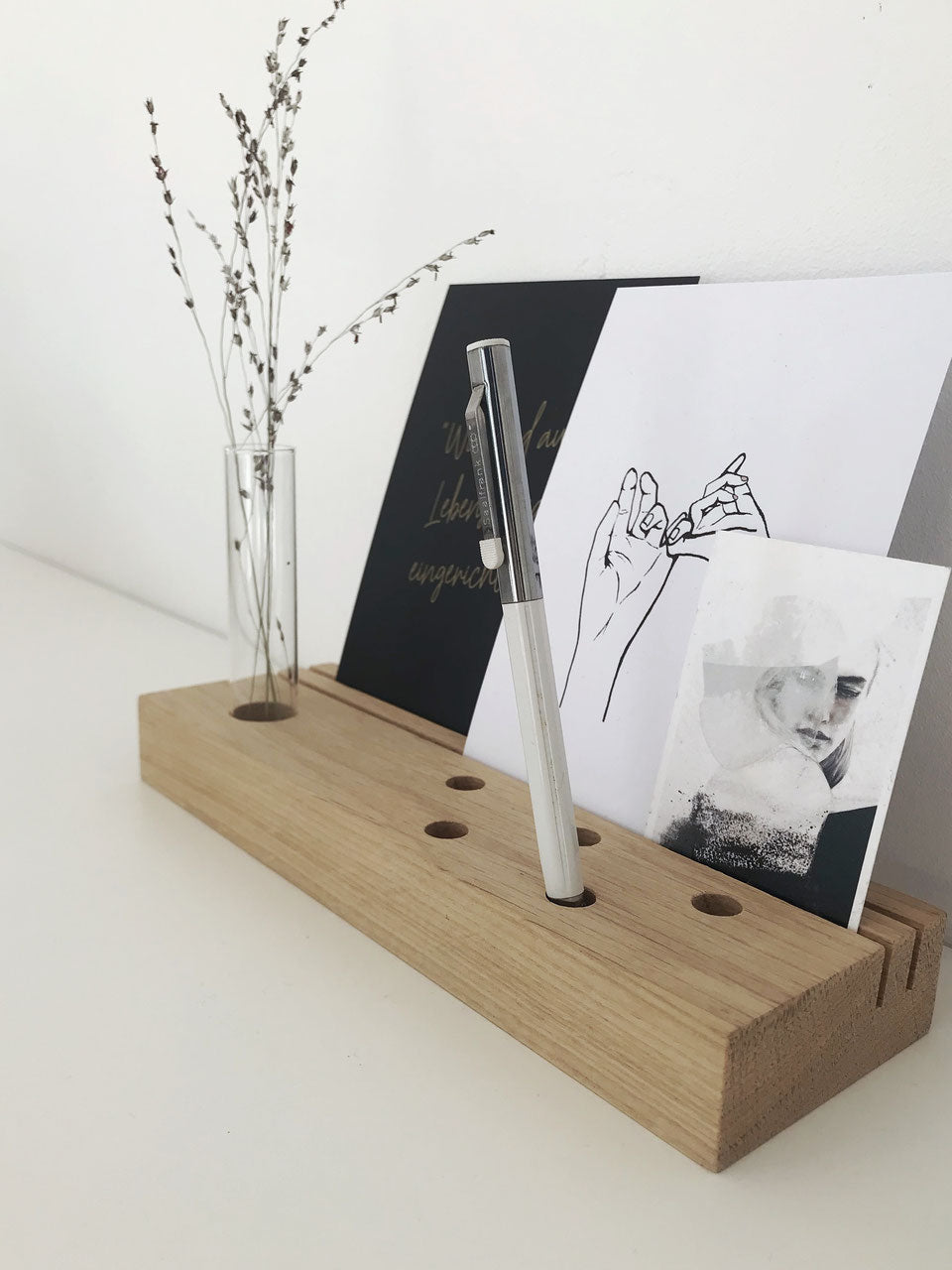 Multifunktionaler Karten-und Stiftehalter mit Platz für ein Reagenzglas, in dem ein Weidenzweig steckt. Dekoriert mit einem Stift, einer Postkarte mit einem Zitat und einer Feder aus Holz