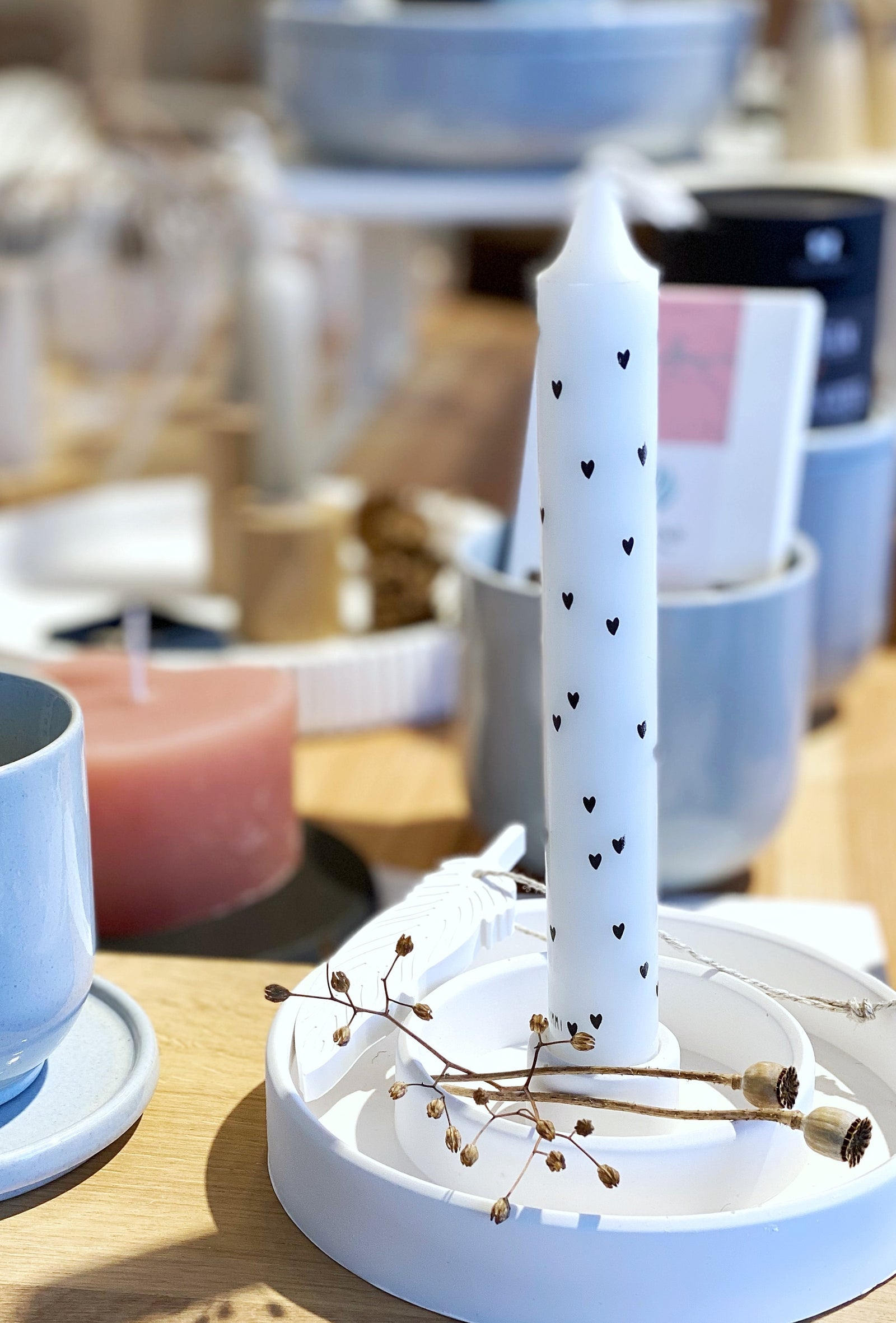 Weißer Kerzenständer, alch mit doppeltem Rand und einer weißen Kerze mit schwarzen Herzen sowie getrockneten Mohnkapseln