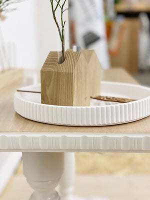 Kleines Blumenhaus aus naturbelassener Eiche mit herausnehmbarem Reagenzglas, in dem ein kleiner Zweig erkennbar ist. Auf einem weißen Dekoteller dekoriert, der auf einem antiken Tische steht