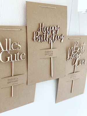 drei Caketopper, aus Holz gelasert auf Natur Karton. Einmal "alles Gute", einmal "Happy Birthday", einmal "Best Day Ever" hängen nebeneinander