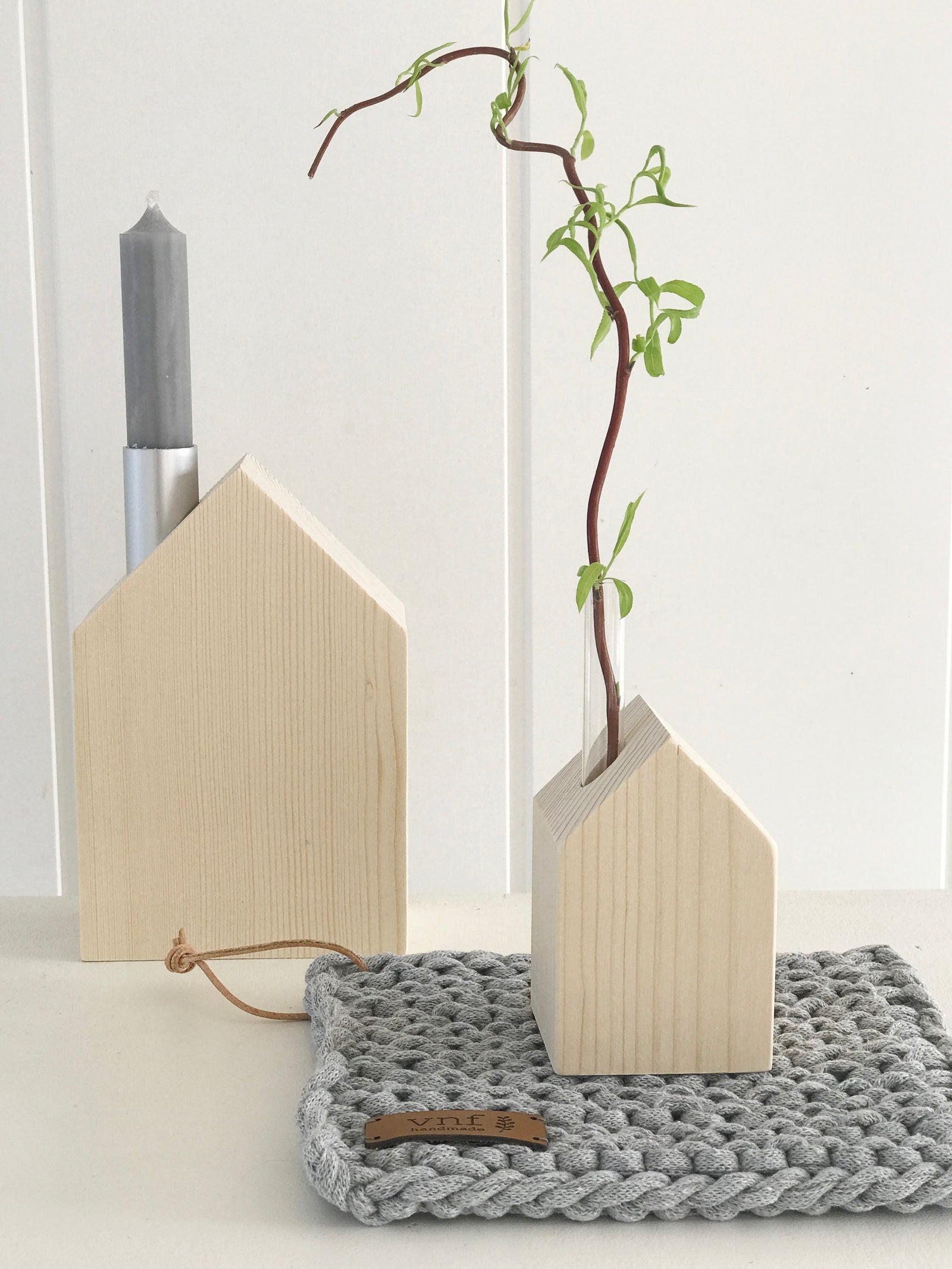 Großes Kerzenhaus und kleines Blumenhaus aus naturbelassenem Fichtenholz, dekoriert mit Kerze und Weidenzweig auf einem gruaen, gehäkeltem Untersetzer