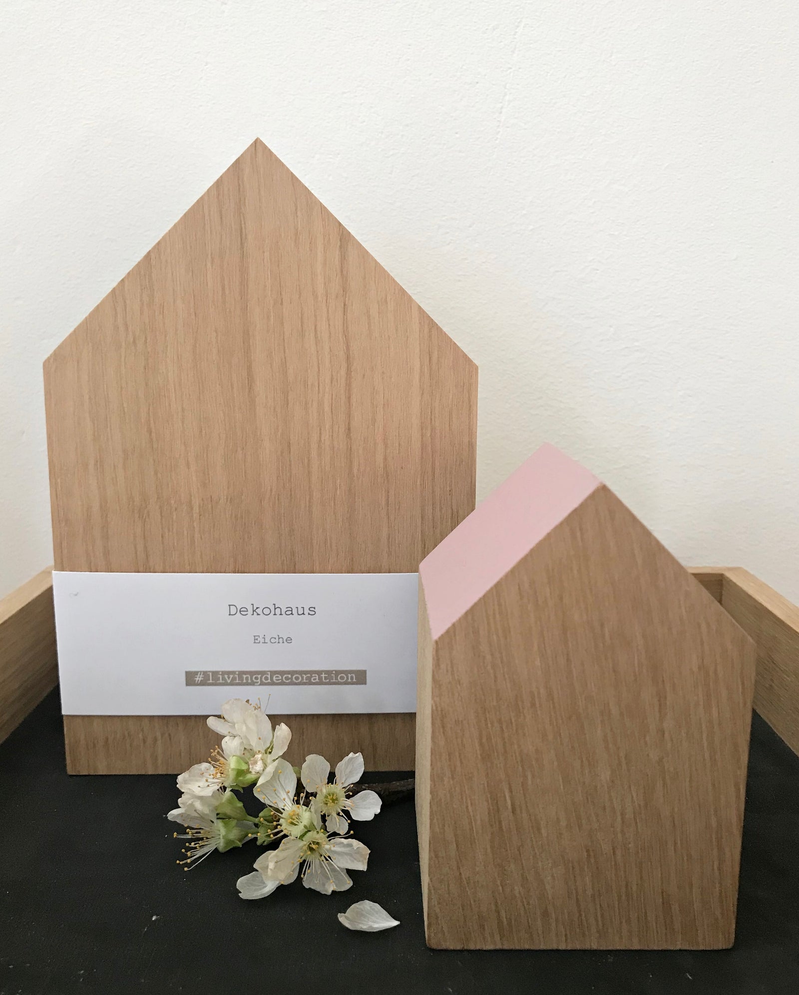 Drei kleine Dekohäuser aus Eichenholz, deren Giebel unterschiedlich lackiert sind. Je einmal in schwarz, rosé und sandstone. Sie stehen auf einem quadratischem Holztabeltt und sind mit einer zarten, kleinen Blume dekoiert