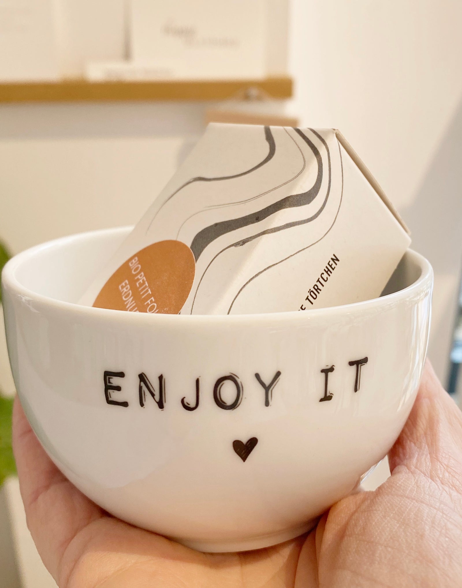 Eiblick in ein Regal im Conceptstore Stadtradstil: mehrer Küchenutensilien im Hintergrund, im Vordergrund zwei weiße, kleine Porzellan schalen mit den Aufdrucken "enjoy it" und "snack it"