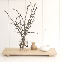 Wohninspiration: im Hintergrund ein graues Sofa mit grauen und weißen Kissen, Trockengräsern. Davor ein schwarzer Metalltisch mit einem Holztablett, einem weißen Kerzenhalter, einer Vase mit Gartenblumen. Natürlich, schlichte Einrichtung