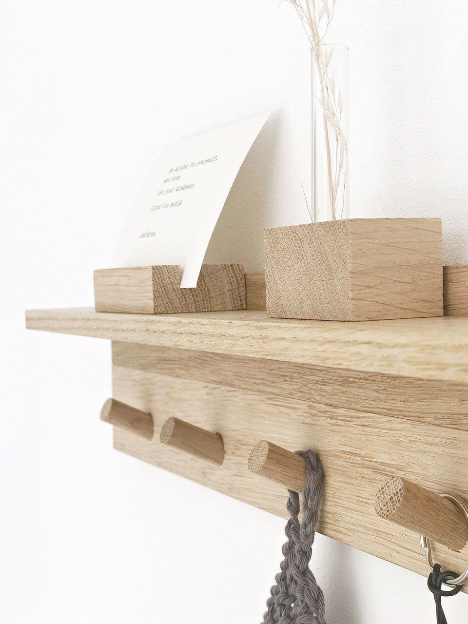 Schrägansicht einer Hakenleiste aus Eiche mit Ablagebord. Darauf steht ein kleiner Kartenhalter mit einer Karte und eine Minivase mit getrocknetem Gras. An den Haken hängz ein Schlüsselanhänger mit einem Minihasu und ein gestricktes dunkelgraues kleines Tuch