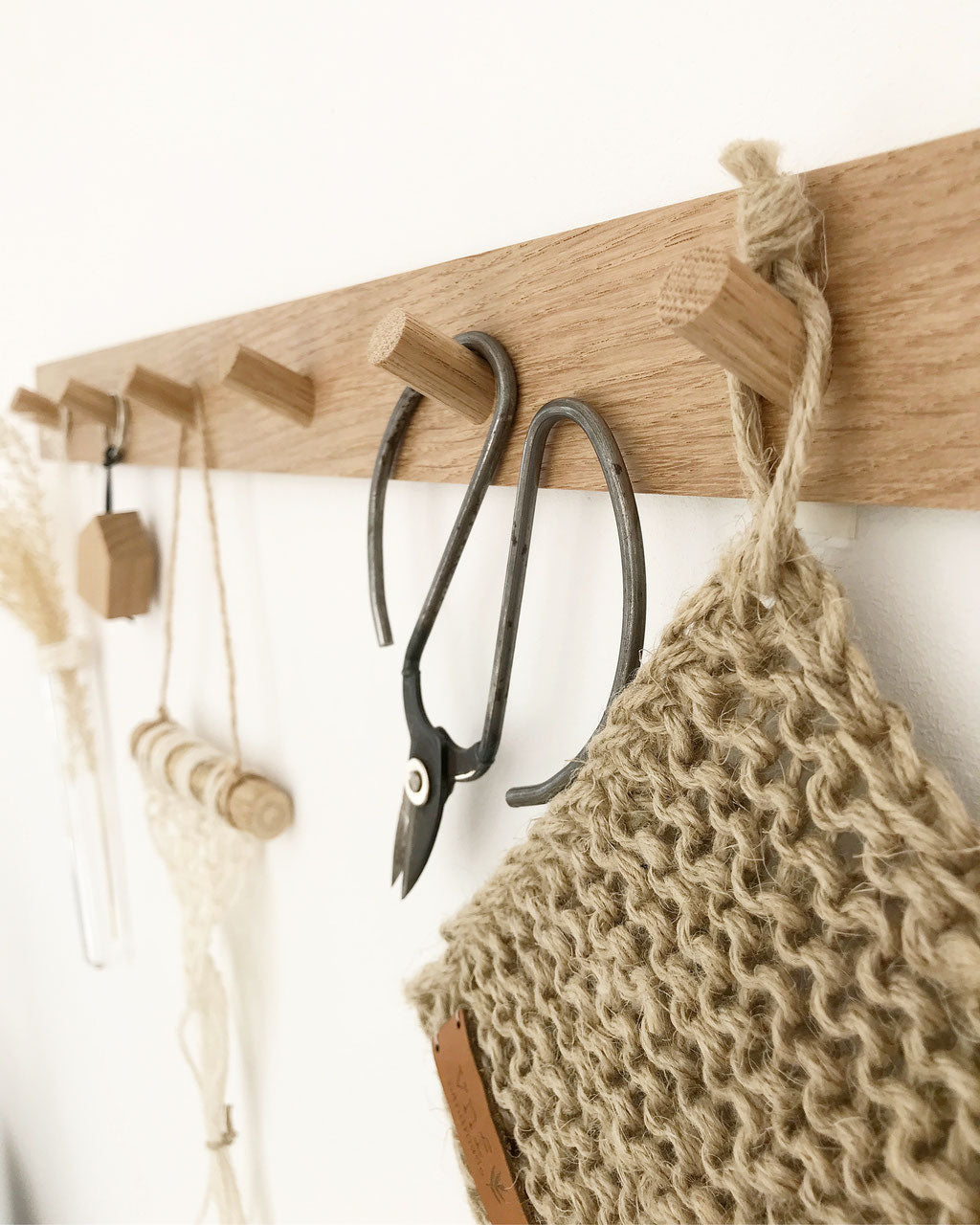 Seitenansicht auf eine lange Hakenleiste aus naturbelassener EIche an der ein Schlsselanhänger, eine Schere und ein Untersezer aus Jute hängen