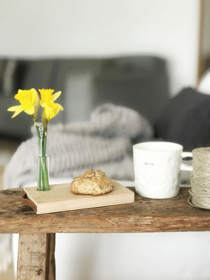 Gemütliche Dekoration mit dem Kerzenbrett forone von Stadtrandstil. Statt Kerze ist ein Reagenzglas mit zwei Narzissen gefüllt, auf dem Brett liegt ein Scone und daneben steht ein weißer Kaffeebecher. Alles zusammen auf einem Schemel aus Altholz