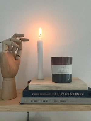 Dekoration Inspiration. Stimmungsvolles Arrangement auf einem Holzbord. Mit Büchern, einem Kerzentablett mit brennender Kerze und einem dunklen Glas. Daneben ein Holzobjet in Handform