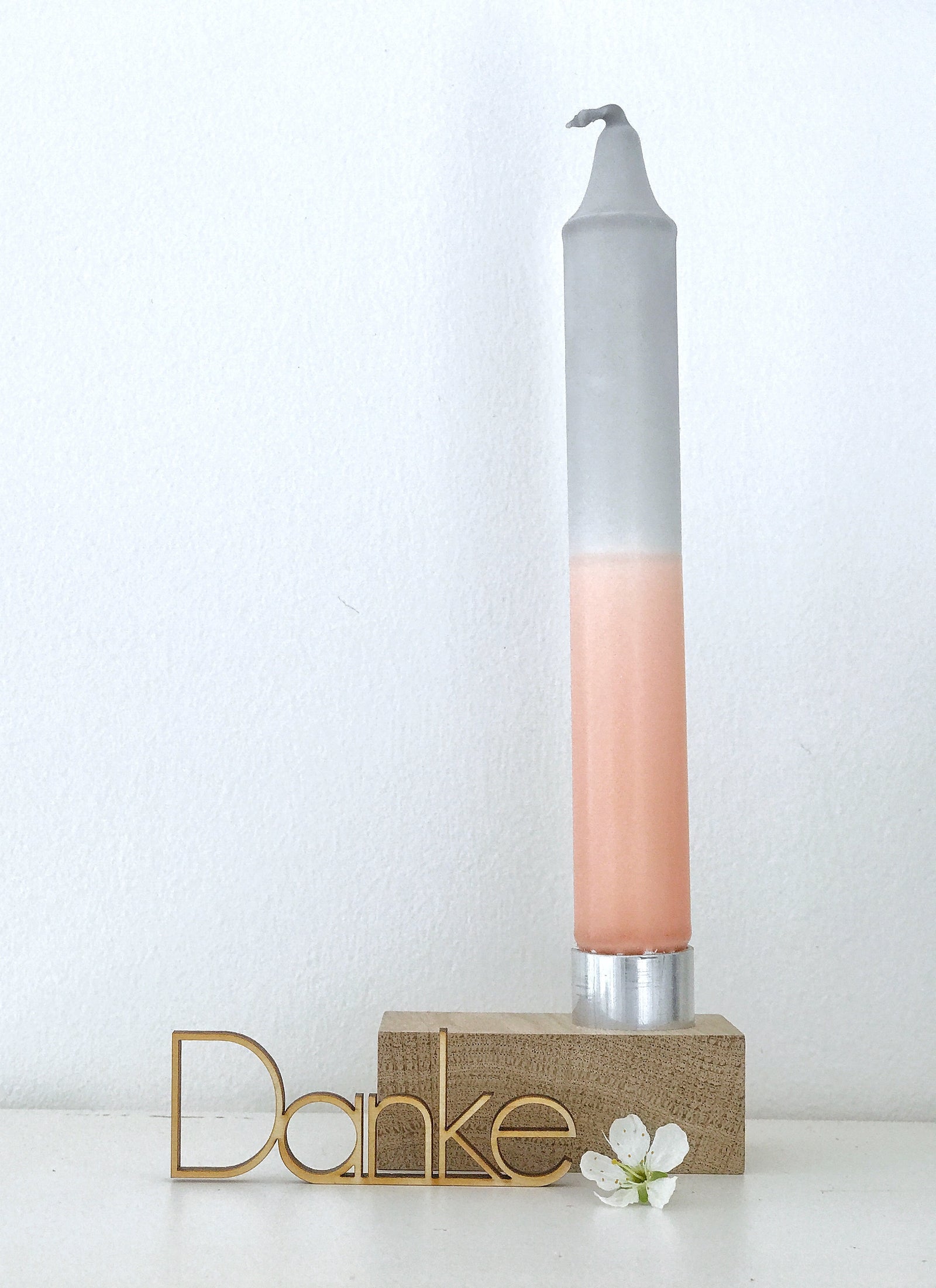 Kleiner, minimalistischer Kerzenhalter aus Eiche mit DipDye Kerze in lachs und grau. Davor ein gelaserter Schriftzug "Danke" und einer einzelnen, weißen Blüte