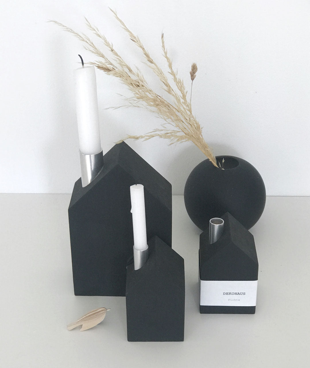 ein großes und zwei schwarze, matte Kerzenhäuser von Stadtrandstil mit weißen Kerzen und einer schwarzen Kugelvase, dekoriert mit getrockneten Gräsern, im Hintergrund