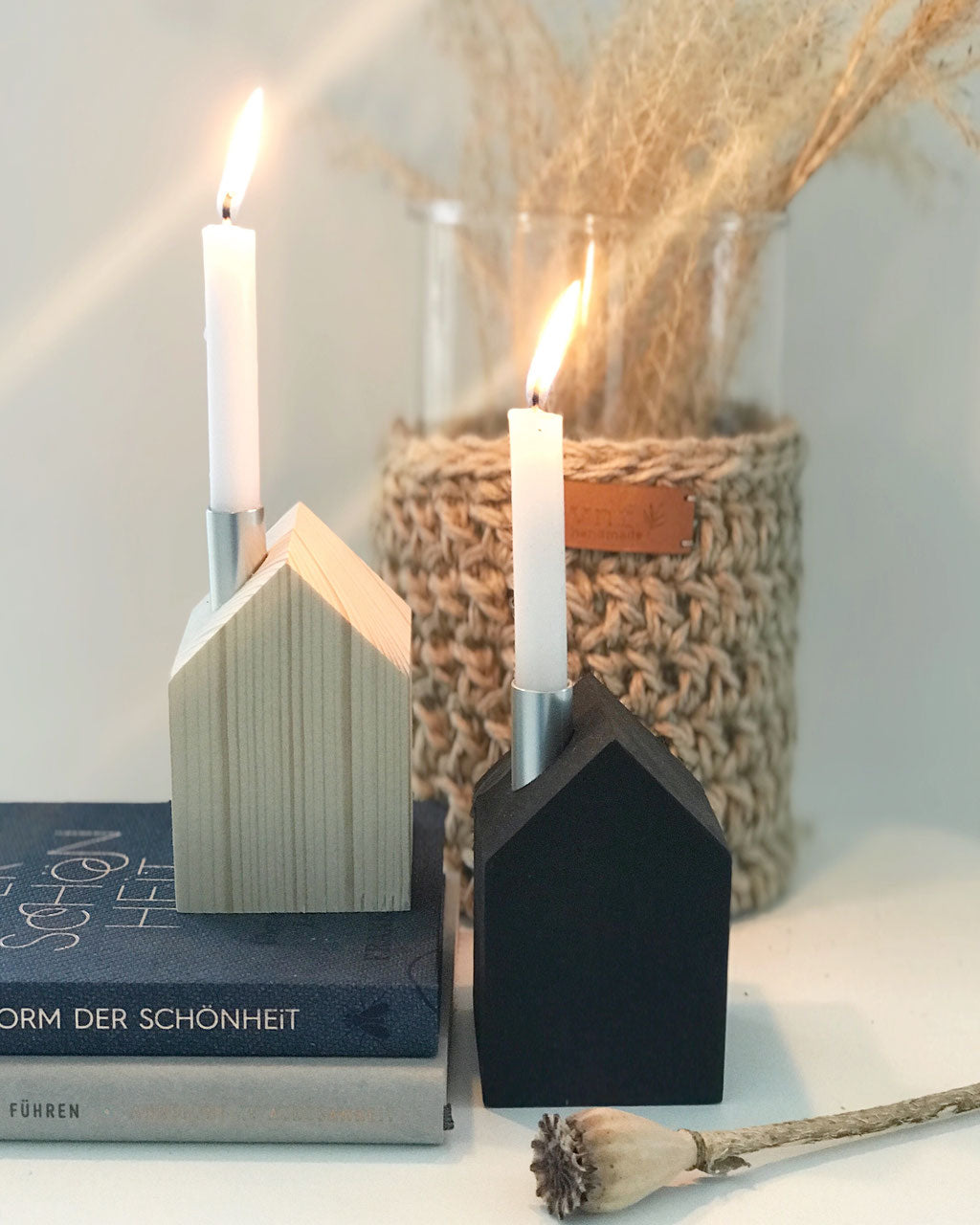 ein großes und zwei schwarze, matte Kerzenhäuser von Stadtrandstil mit weißen Kerzen und einer schwarzen Kugelvase, dekoriert mit getrockneten Gräsern, im Hintergrund