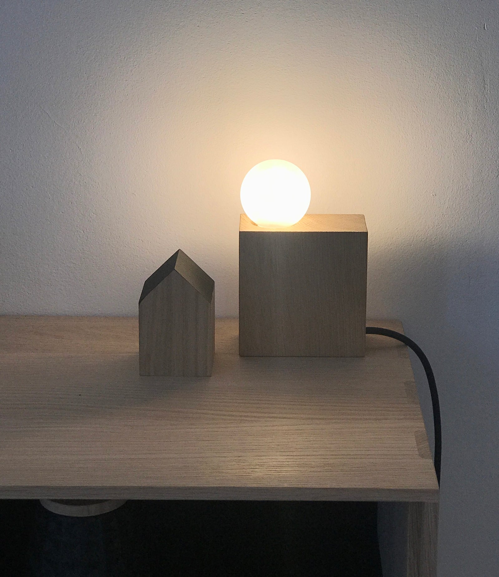 Minimalistische Lampe aus einem quadratischen Eichenblock und runder Milchglas Lampe, daneben Bücher