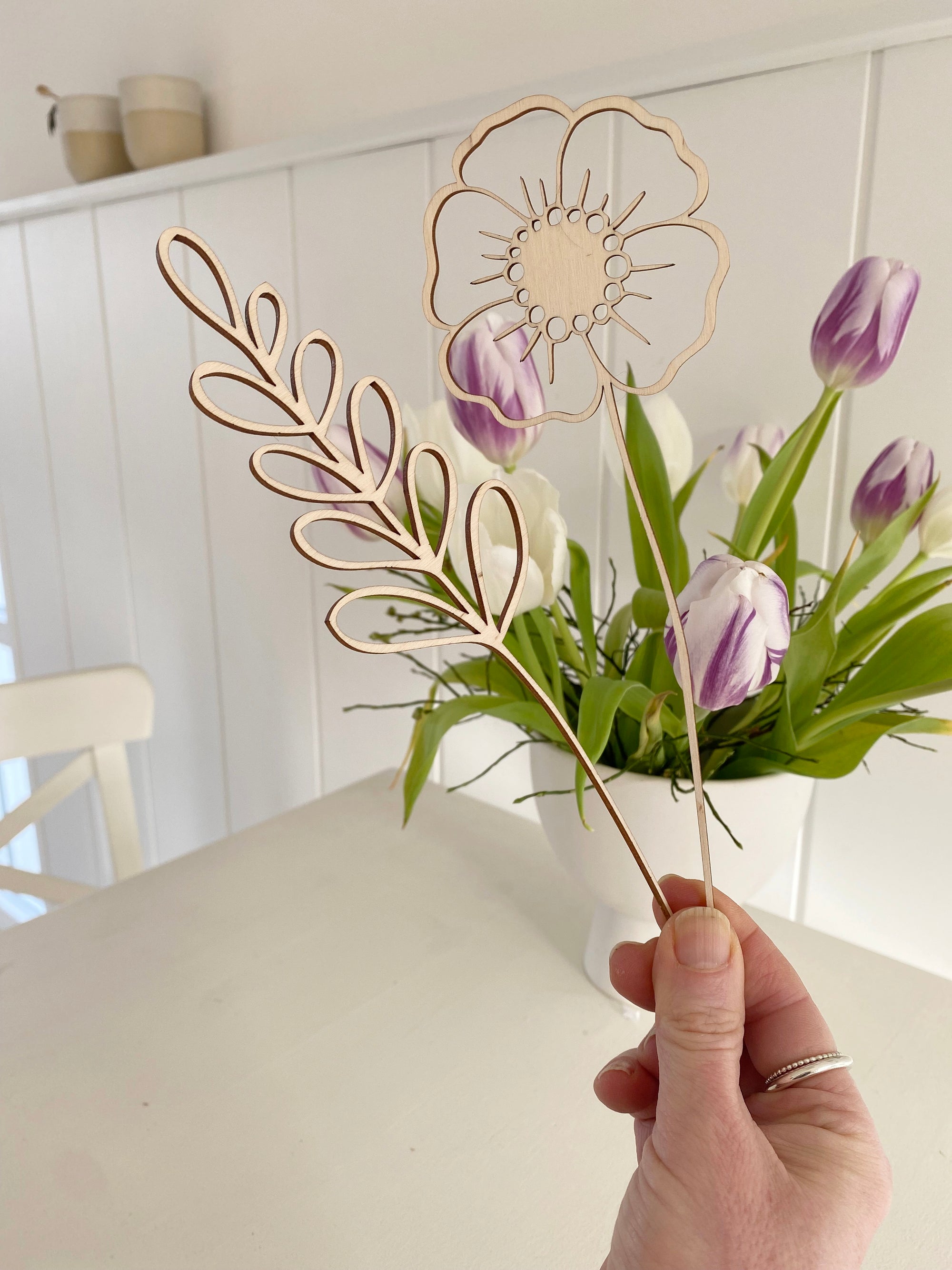 Schlichte Dekoration: minimalistisches Blumendisplay aus Holz, gefüllt mit Trockengräsern und Holzblumen vor weißem Hintergrung