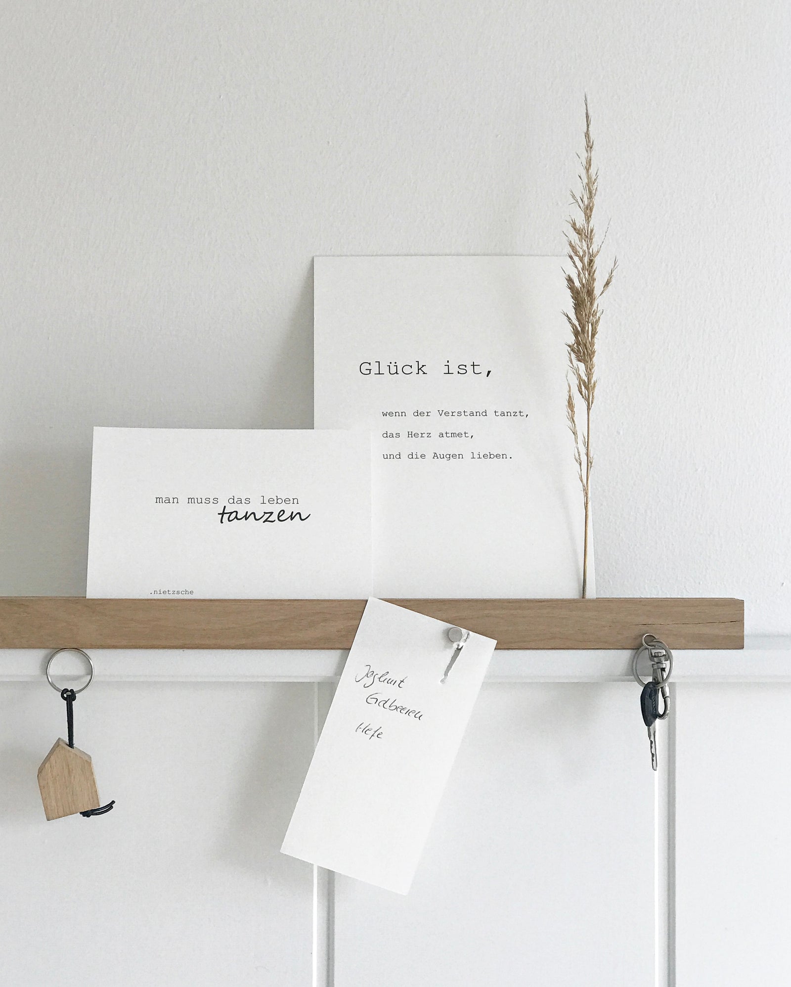 Wandleiste von Stadtrandstil handmade, natürlich und zeitlos dekoriert mit weißen Postkarten mit Text, einem getrocknetem Gras, einem Einkaufzettel. Fahrradschlüssel und einem Schlüsselanhänger in Hausform