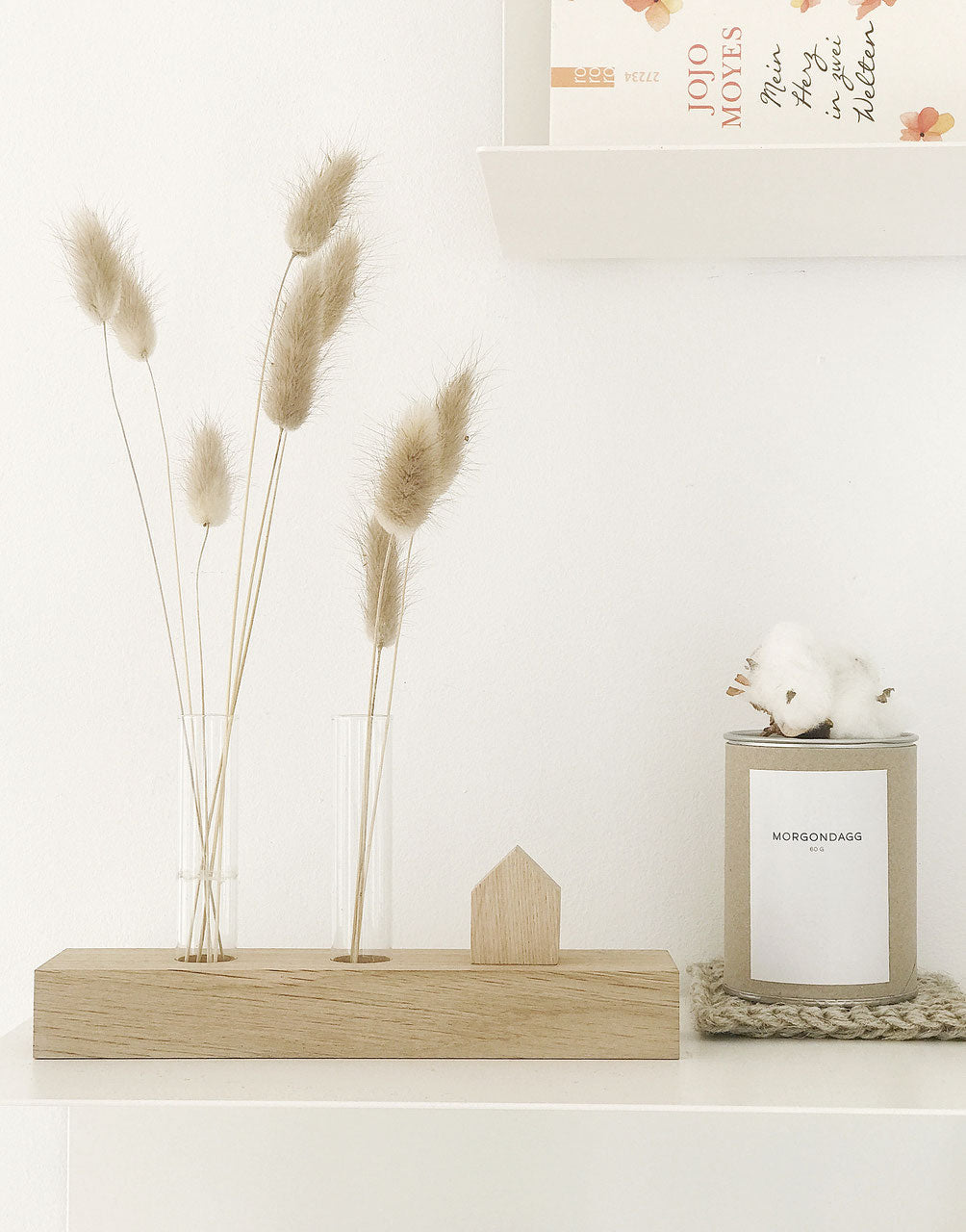 Dekoidee: Minihaus auf Blumenwiese, die mit Hasenschwänzchen gefüllt sind. Daneben eine naturfarbene Dose auf einem Untersetzer aus Jute.