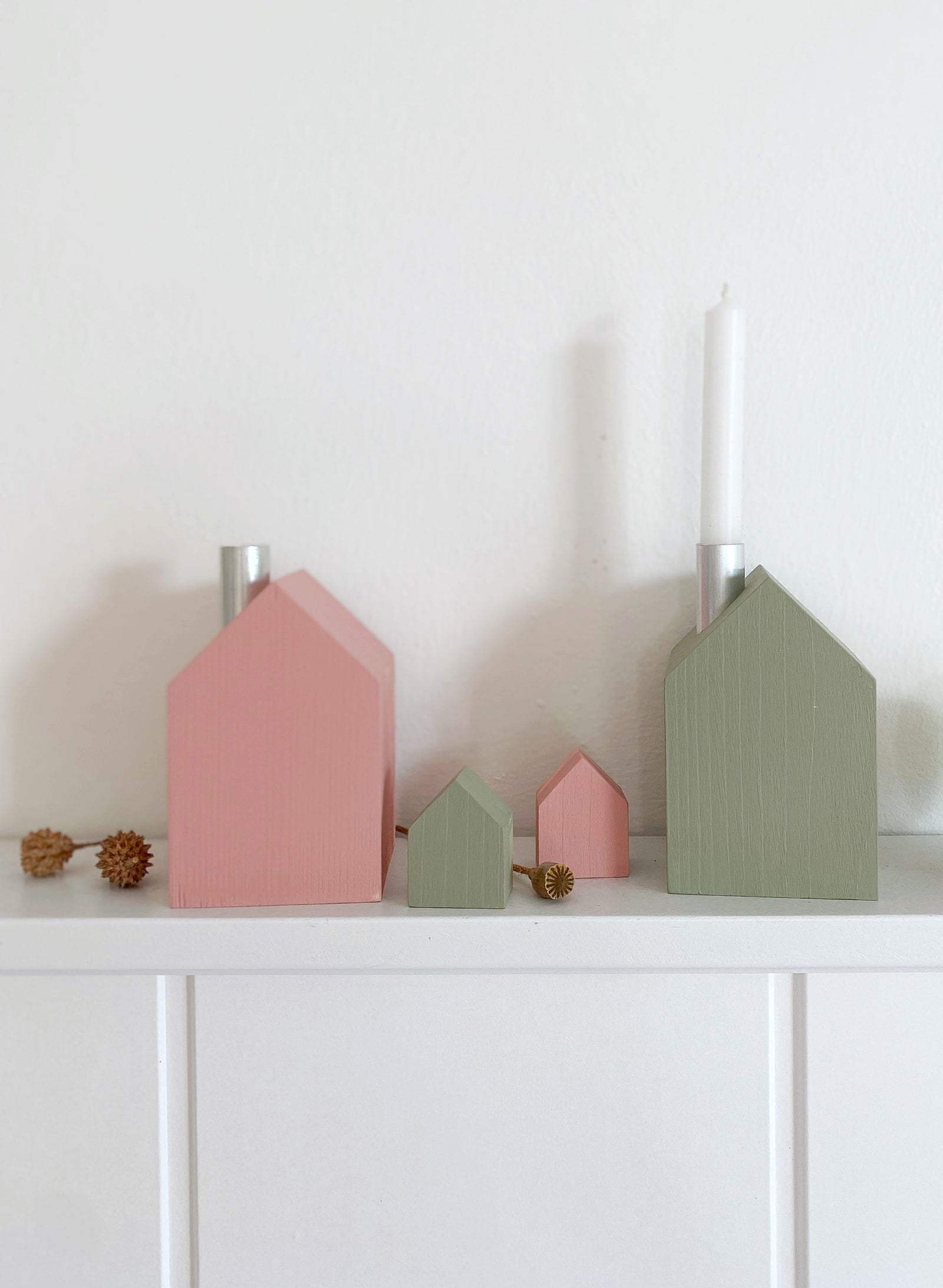 Zwei bunte Kerzenhäuser mit weißen Kerzen, eines in rosé, eines in oliv. Davor eine getrocknete Hortensienblüte