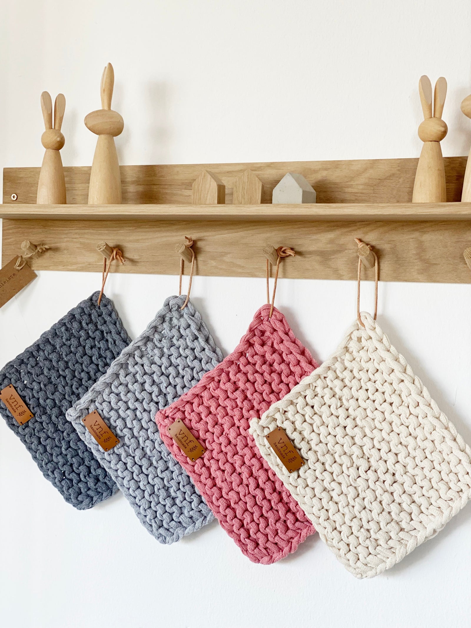 Eichenleiste mit Ablage an der vier gestrikte Untersetzer hängen. Auf der Ablage stehen minimalistische Hasen und drei Minihäuser. Alles von Stadtrandstil handmade