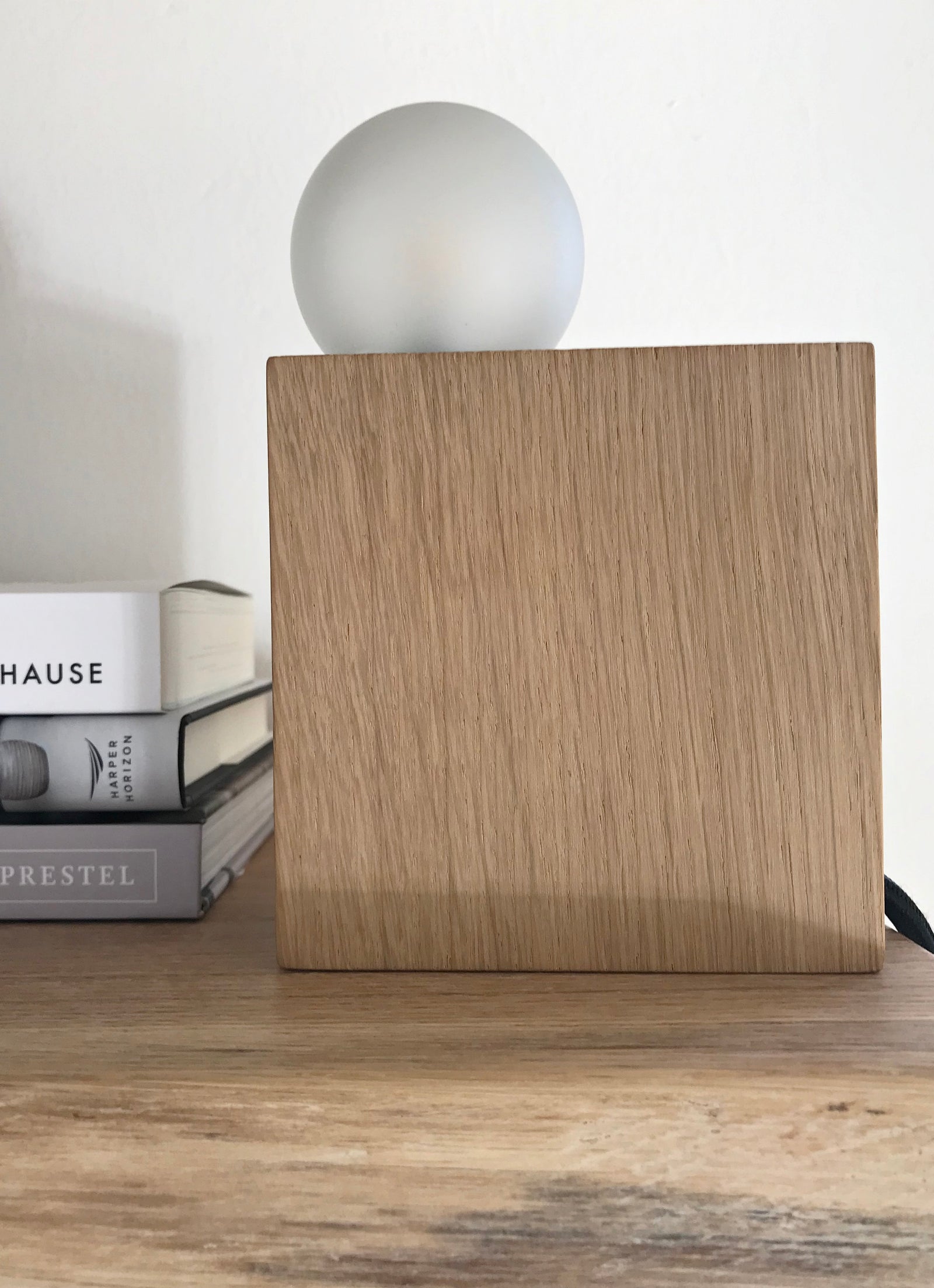Minimalistische Lampe aus einem quadratischen Eichenblock und runder Milchglas Lampe, daneben Bücher