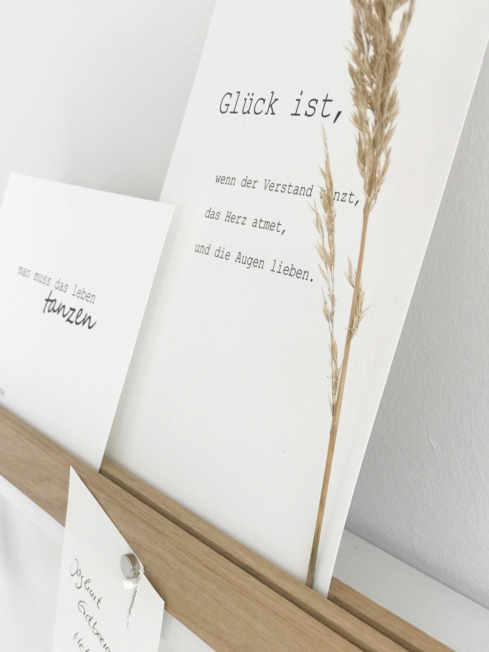 Wandleiste von Stadtrandstil handmade, natürlich und zeitlos dekoriert mit weißen Postkarten mit Text, einem getrocknetem Gras, einem Einkaufzettel. Fahrradschlüssel und einem Schlüsselanhänger in Hausform